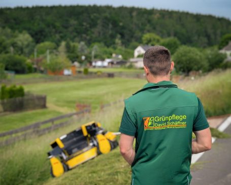 Grasmahd zur Landschaftspflege mit Mähraupe und Rasenmäher an Steilhang und Böschungen